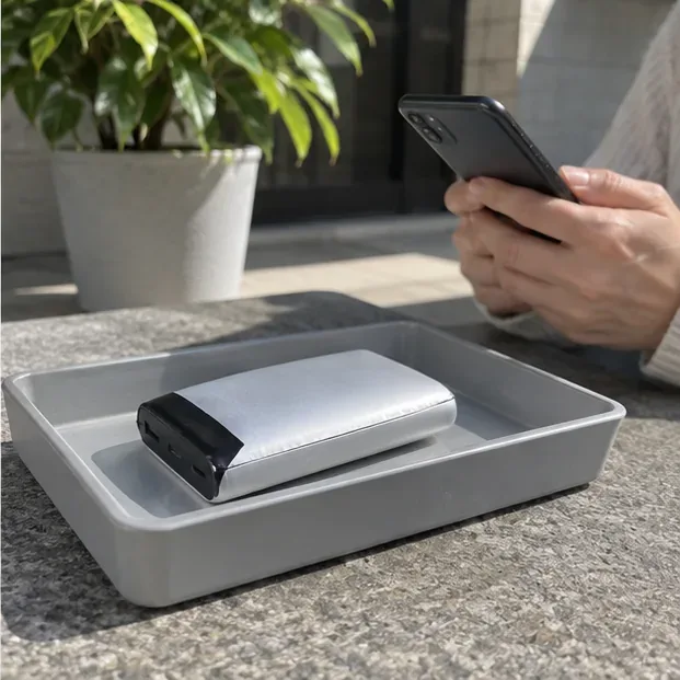 膨らんだモバイルバッテリーを平らなトレーに置き、スマートフォンで浜松市の収集日や搬入情報を確認している場面