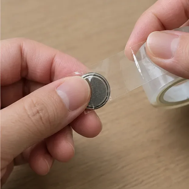 小さな丸形電池の金属端子を透明なテープで覆い、絶縁している手元