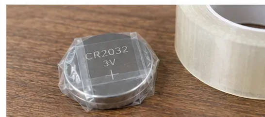 CR2032と表示された丸い電池の表面と側面を透明なテープで覆い、横に透明テープのロールが置かれている様子
