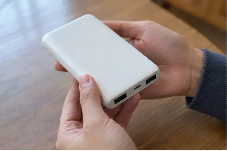 白いモバイルバッテリーを両手で持ち、表面や端子付近に膨張や破損がないか確認している様子