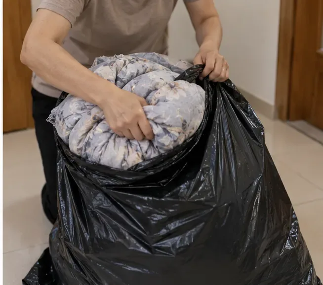 住戶把摺好的花色棉被裝進大型黑色垃圾袋，讓棉被不鬆散外露