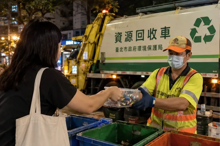 夜間街道旁，民眾把一盒廢電池交給資源回收車旁的清潔人員