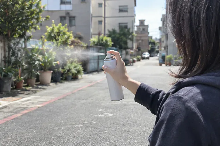 女子在戶外空曠街道持白色噴霧罐向無人的方向排放剩餘內容物
