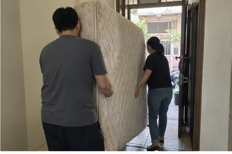 兩名住戶一起把大型床墊直立搬過室內走道，準備移到一樓