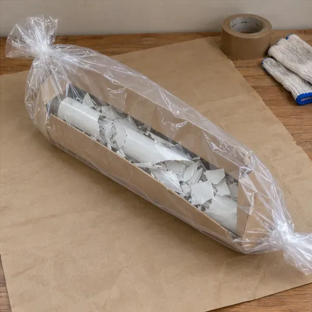 破損日光燈管與碎片收在厚紙板包裝及外層塑膠袋內，置於桌面上