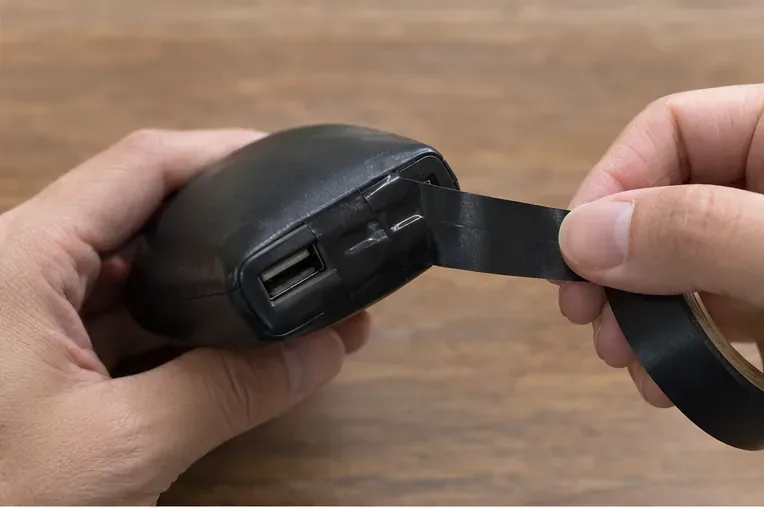 膨らんだ黒いモバイルバッテリーの端子部分に絶縁テープを貼っている手元