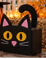 Scatola per gatti in cartone nero con orecchie a punta, occhi gialli, naso rosa e coda arricciata
