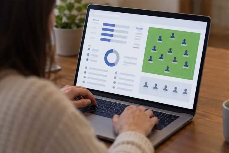 Pessoa usa um notebook com um painel genérico de estatísticas e uma formação de futebol representada em um campo.