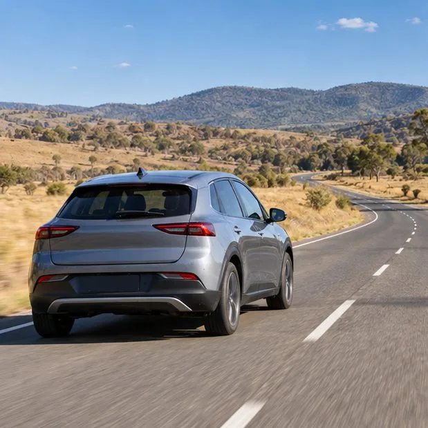 A gray electric car travels on a quiet road through open countryside.