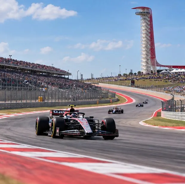 Una monoposto affronta una curva su un circuito con tribune e una torre panoramica sullo sfondo.