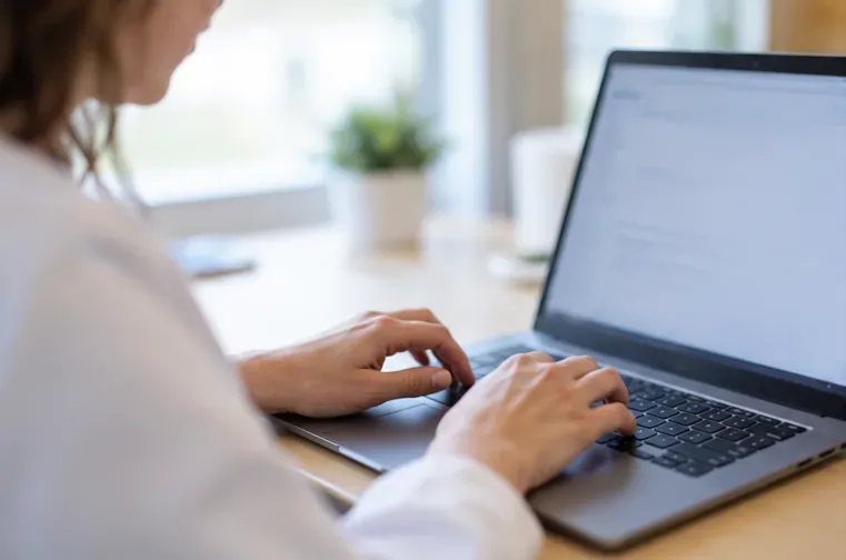 Mains d’un professionnel saisissant un message sur un ordinateur portable, écran sans texte lisible
