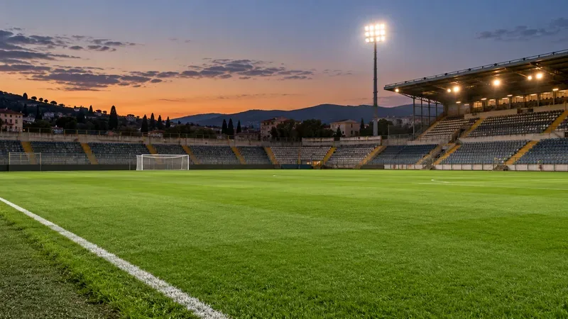 Un campo da calcio vuoto al crepuscolo, con le linee bianche, una porta e gli spalti illuminati.
