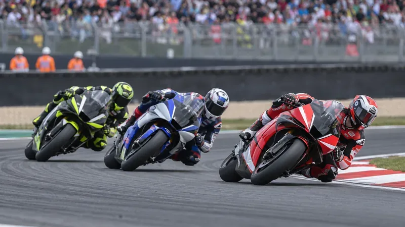 Drie Grand Prix-motoren met coureurs liggen schuin in een bocht, met baanposten achter de vangrail.