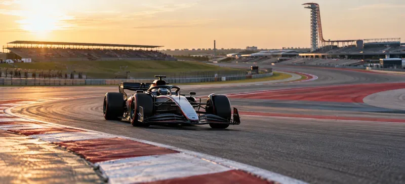 A single-seater race car entering a circuit corner beside red-and-white kerbing